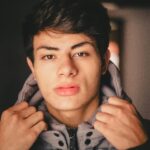 Close-up portrait of a young man adjusting his jacket indoors.